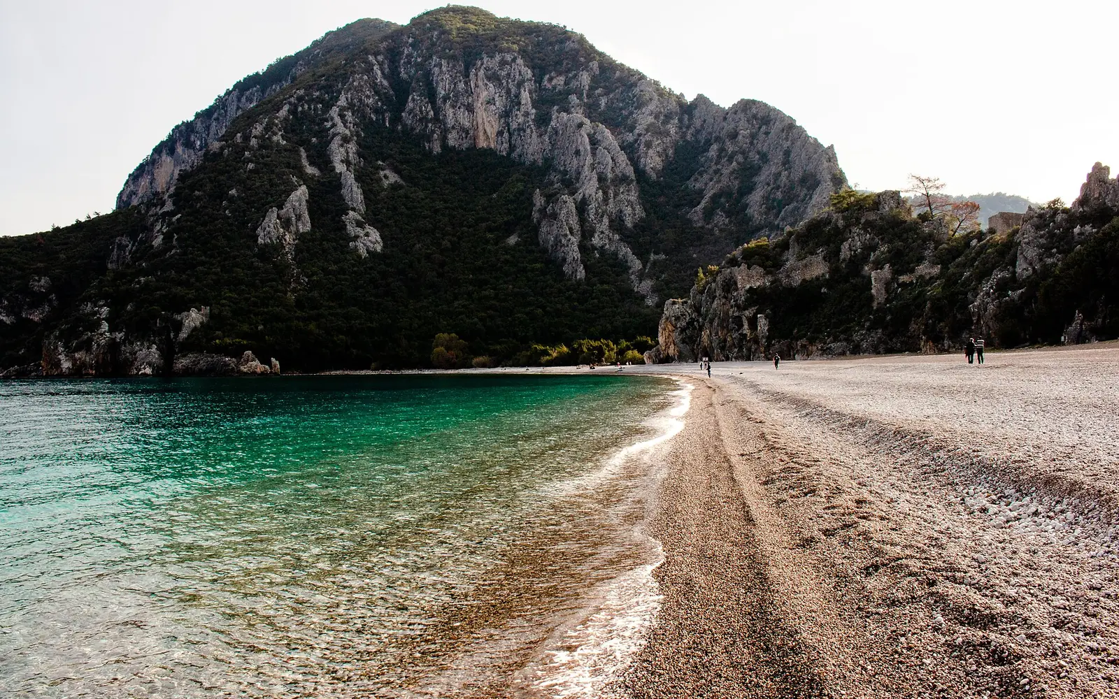 Çıralı Plajı ve çakıl kıyının ardındaki Olympos kayalığı